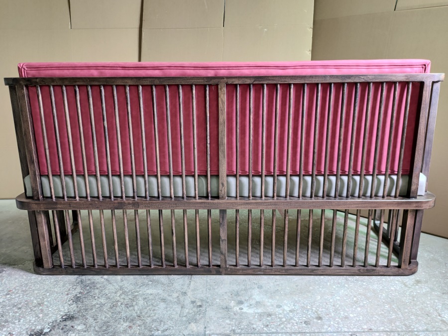 Back view of solid wood booth sofa for restaurant with pink backrest, grey seat cushion, and vertical wooden slats