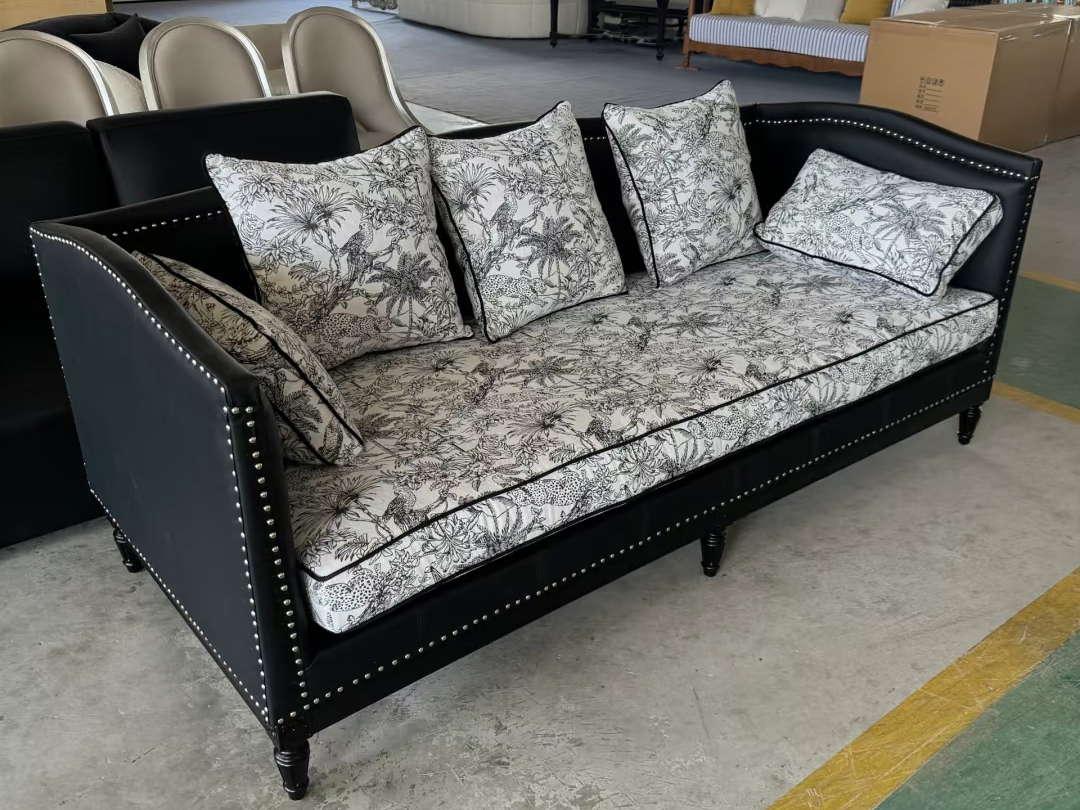 Black leather vintage sofa with botanical print cushions in factory setting