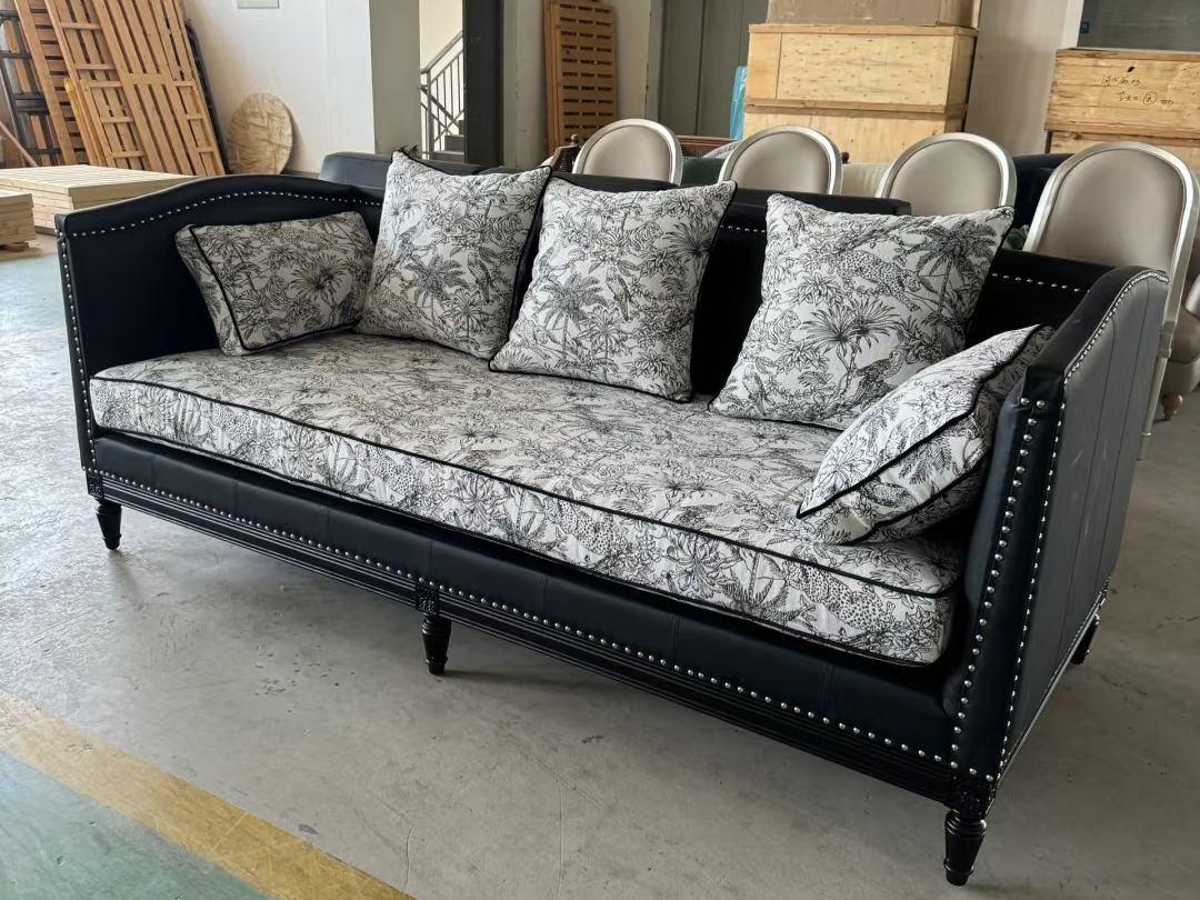 Black leather vintage sofa with botanical print cushions in factory setting